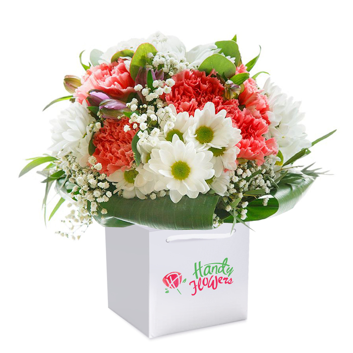 Upright in a flawless white gift bag, this sumptuous bouquet is a true showcase of sophisticated Nine Elms floristry. A vibrant mosaic of coral and peach carnations, noted for their lush, ruffled petals, is complemented by clusters of pristine white daisy chrysanthemums-each crowned with a luminous lime-green center, together evoking the riverside vitality of Nine Elms. Airy sprays of white gypsophila meander among the central blooms, offering softness and depth akin to mist drifting over the Thames on a bright morning. Encasing the composition, broad, glossy leaves of deep green gracefully arc, forming a supportive base reminiscent of the landscaped gardens nearby. Scattered within, a few tightly closed purple-tinged buds hint at evolving beauty and the unfolding dynamism found around Embassy Gardens. The bouquet is completed with a smart white gift bag furnished with ribbon handles, perfect for easy, elegant delivery to addresses across Nine Elms. Illuminated by delicate, even lighting, the arrangement's full, rounded shape and nuanced palette are brought vividly to life, presenting a fresh, uplifting option for every occasion-from birthdays to new beginnings. Every stem reflects the skilled touch of hardworking local florists, ensuring genuine Nine Elms quality in every blossom.