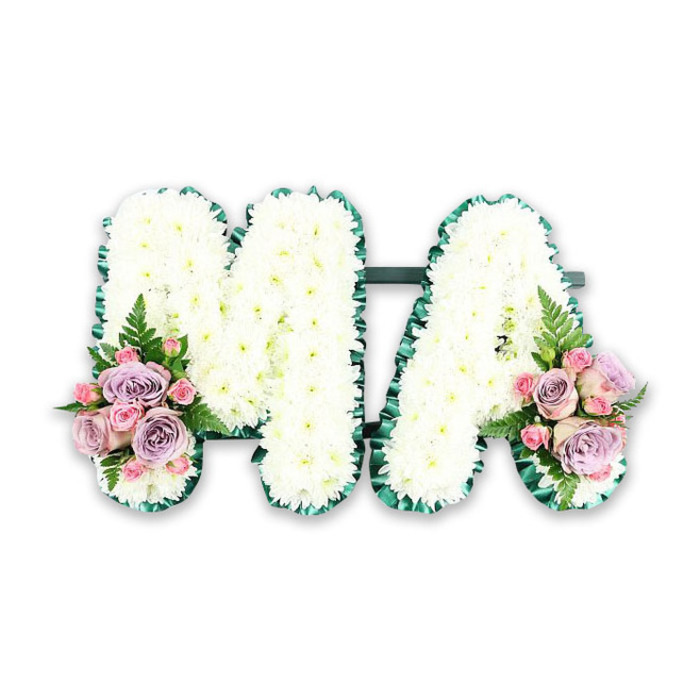 A meticulously arranged memorial spells out MA in dense white blooms, likely chosen for their classic sympathy character and soft, tactile appearance. Hundreds of small white chrysanthemums are set edge-to-edge to create a uniformly textured surface that seems almost billowy to the touch, while a vivid, emerald-green satin ribbon defines the outline of each letter with a delicate, ruffled edge that contrasts the white like a frame. The M and A are subtly linked by a dark green horizontal bar so they read as one cohesive tribute rather than two separate initials. Symmetrical floral clusters sit at the lower corners: pale lavender or muted purple roses mingle with blush pink roses and smaller pink spray roses, each cluster finished with a single, feathery fern frond that introduces an airy, natural rhythm. Under soft studio lighting the petals catch a gentle sheen, revealing the roses' layered texture and the chrysanthemums' rounded forms; the overall palette is tranquil-white, soft pinks and muted violet softened by the deep green trim. Intended for a bereavement service, this composition communicates a message of love for a mother, 'Mama' or a dearly missed relative, offering visual comfort and dignity. As a local design, it reflects the quiet attention we give to memorial flowers for families around Nine Elms, Battersea and the riverside chapels, where a thoughtful tribute like this can carry a final, consoling message.