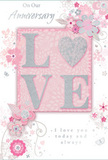 This anniversary card is captured as if resting on a polished table in a Nine Elms home, glowing softly in ambient light. The central feature is the word LOVE, set in large capital letters that rise slightly from the surface, each stroke dusted with fine, shimmering glitter. The effect is tactile and visually striking, like light catching on the edge of fresh petals in a beautifully arranged bouquet. Behind and around the letters, the background transitions through delicate shades of blush pink and pearl white, with a whisper of silver that lends a soft, romantic sheen. Encircling the central motif, a cascade of illustrated flowers and leaves winds gracefully across the card, their outlines thin and controlled, as if drawn by a florist mapping out an anniversary design with roses and soft filler blooms. Some blossoms appear fully formed, petals shaded with gentle gradients of pink, ivory, and grey; others are just hints-curves, spirals, and flourishes that suggest movement and air. Tiny glints of glitter and subtle metallic touches punctuate the design, adding quiet glamour without disturbing the calm mood. A tender anniversary message, written in an elegant script with flowing, looping strokes, frames the floral artwork and reinforces the sense of heartfelt devotion. The surface textures alternate between smooth, satin areas and the slightly rough, raised glitter, inviting gentle touch. Overall, the card feels like a modern, romantic gesture suited to the riverside calm of Nine Elms, the paper equivalent of a thoughtfully curated anniversary bouquet delivered to mark another year of shared memories and love.